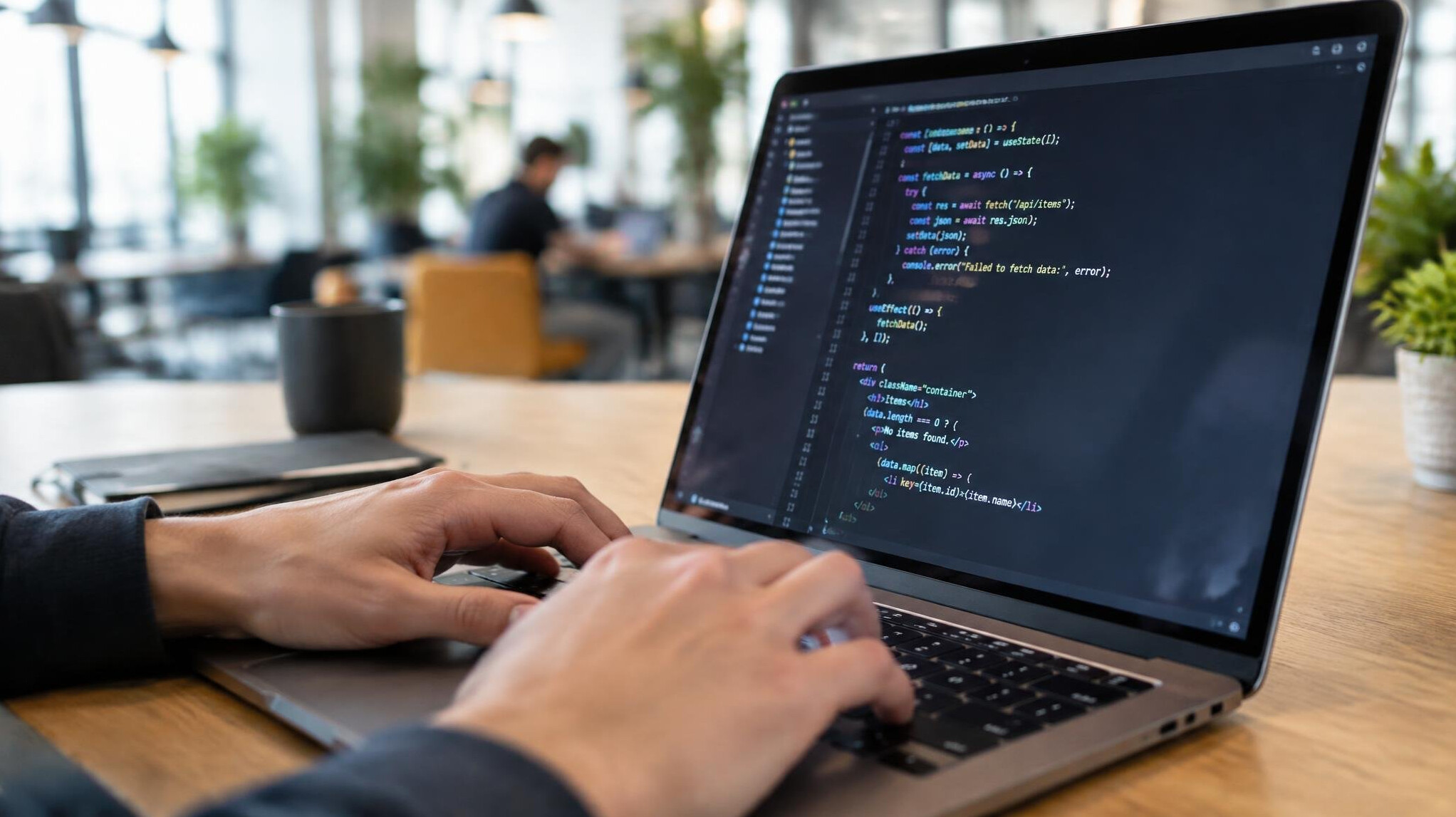 Close-up of hands typing on a laptop keyboard with code on the screen